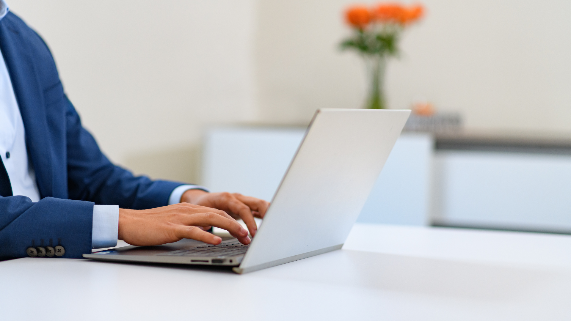 Hände einer Person beim Tippen auf einem Laptop an einem Schreibtisch.
